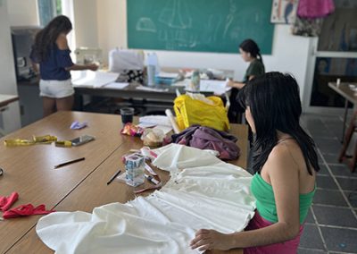 Elaboración de prendas para la clase de corte y confección. Se muestran 3 alumnas con sus telas sobre las mesas de corte.